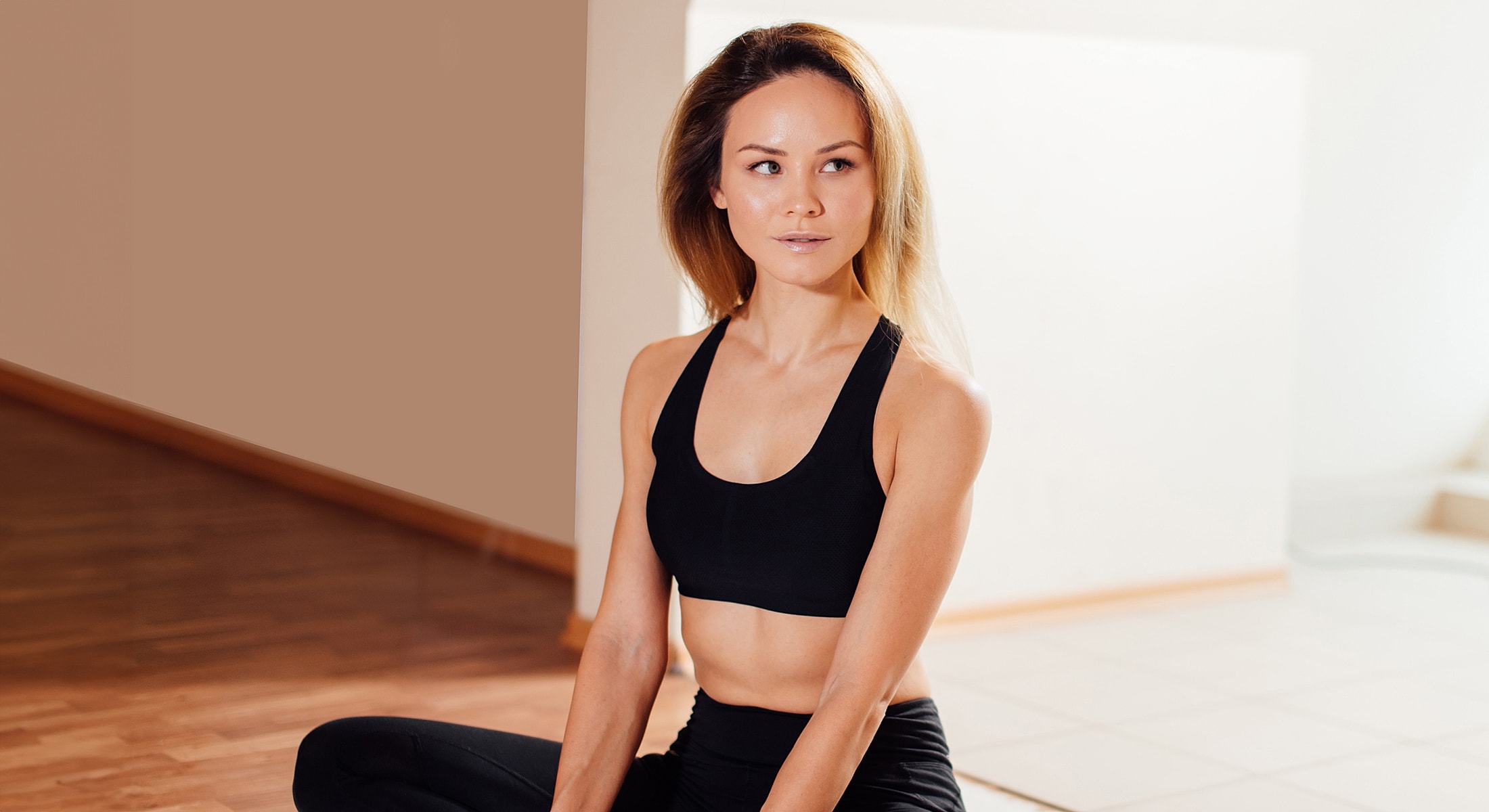 Woman in sportswear sitting indoors, looking thoughtful.